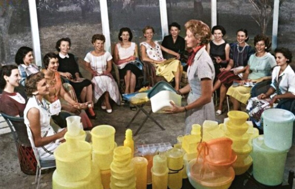 A vintage Tupperware party demonstration, women gathered around stacked containers